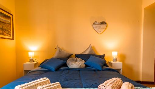 Camera accogliente con letto blu, luci soffuse e asciugamani arrotolati.